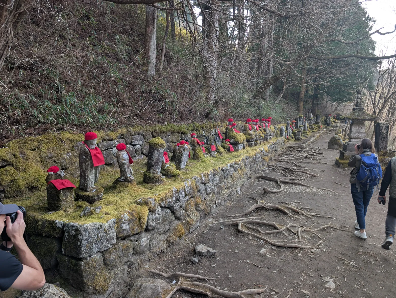 Fila de estatuas Jizo cubiertas de musgo con baberos y gorros rojos a lo largo del sendero de Kanmangafuchi