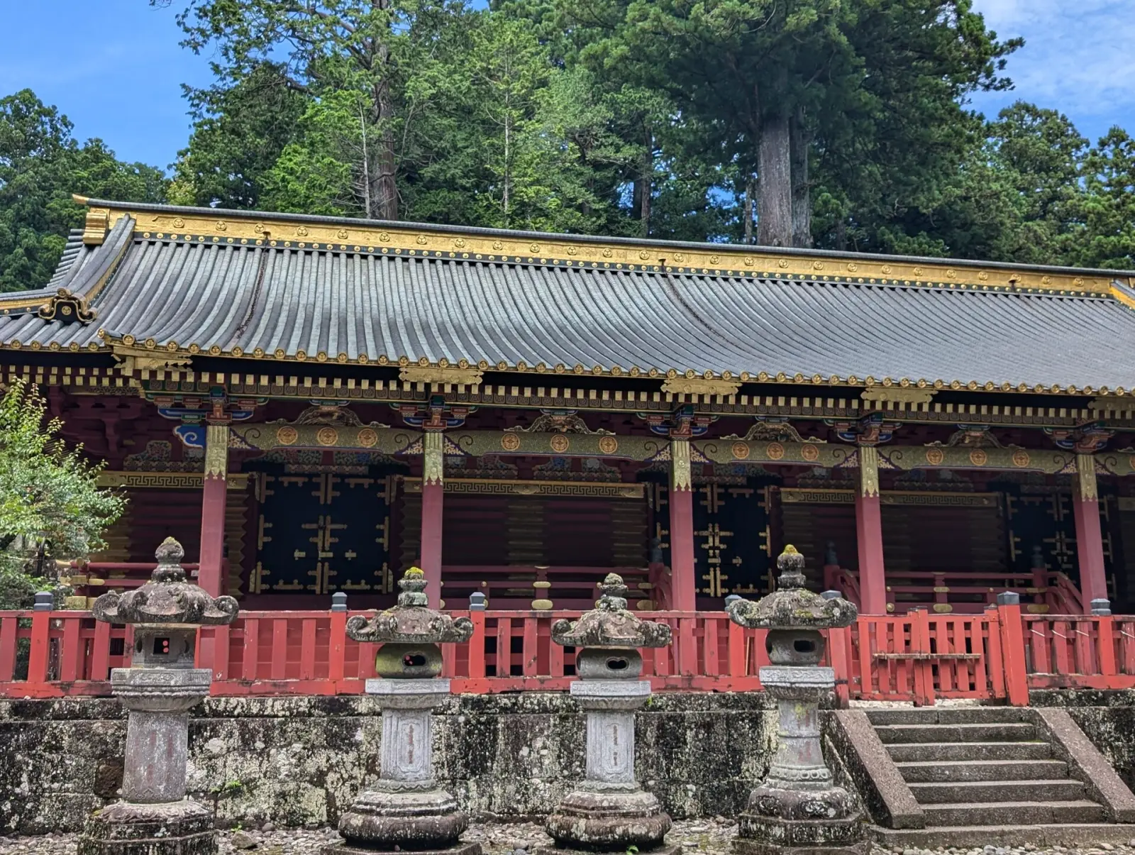 Ornate Buddhist temple hall at Nikko with red pillars, gold trim, and stone lanterns