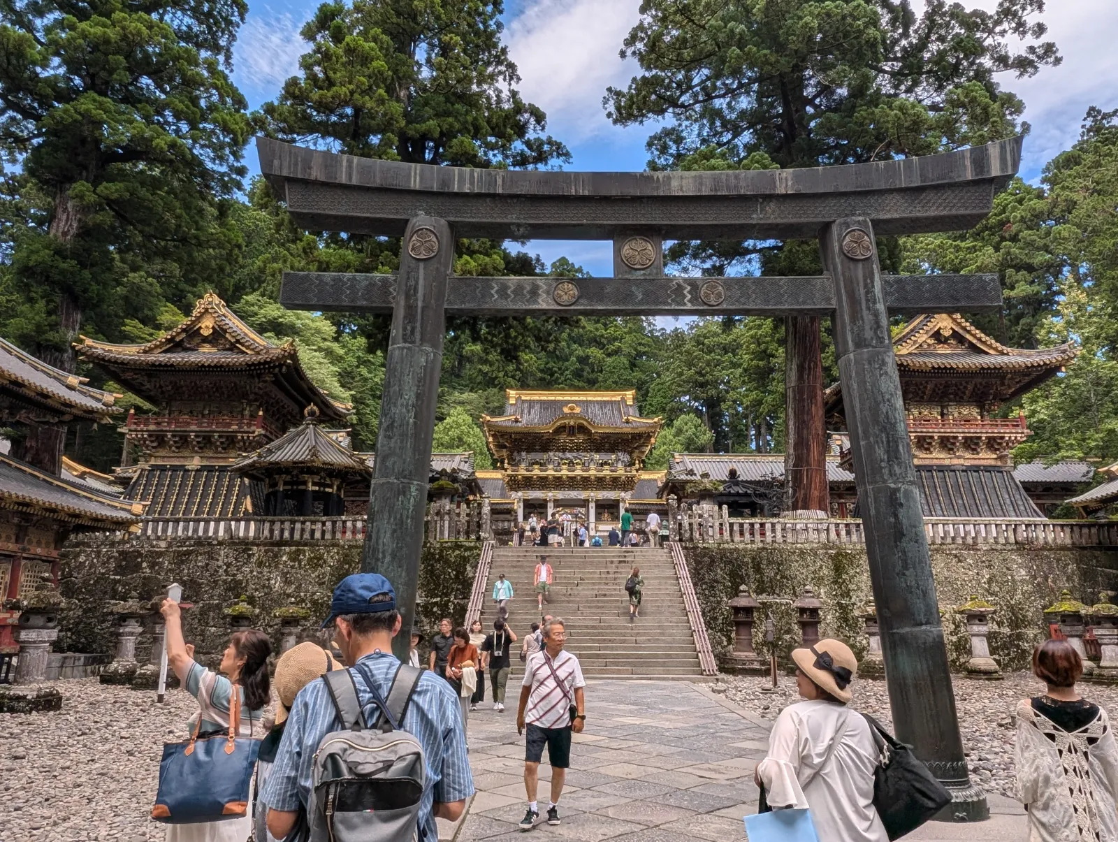 Visitors walking through the stone torii gate toward Tosho-gu Shrine in lush summer greenery