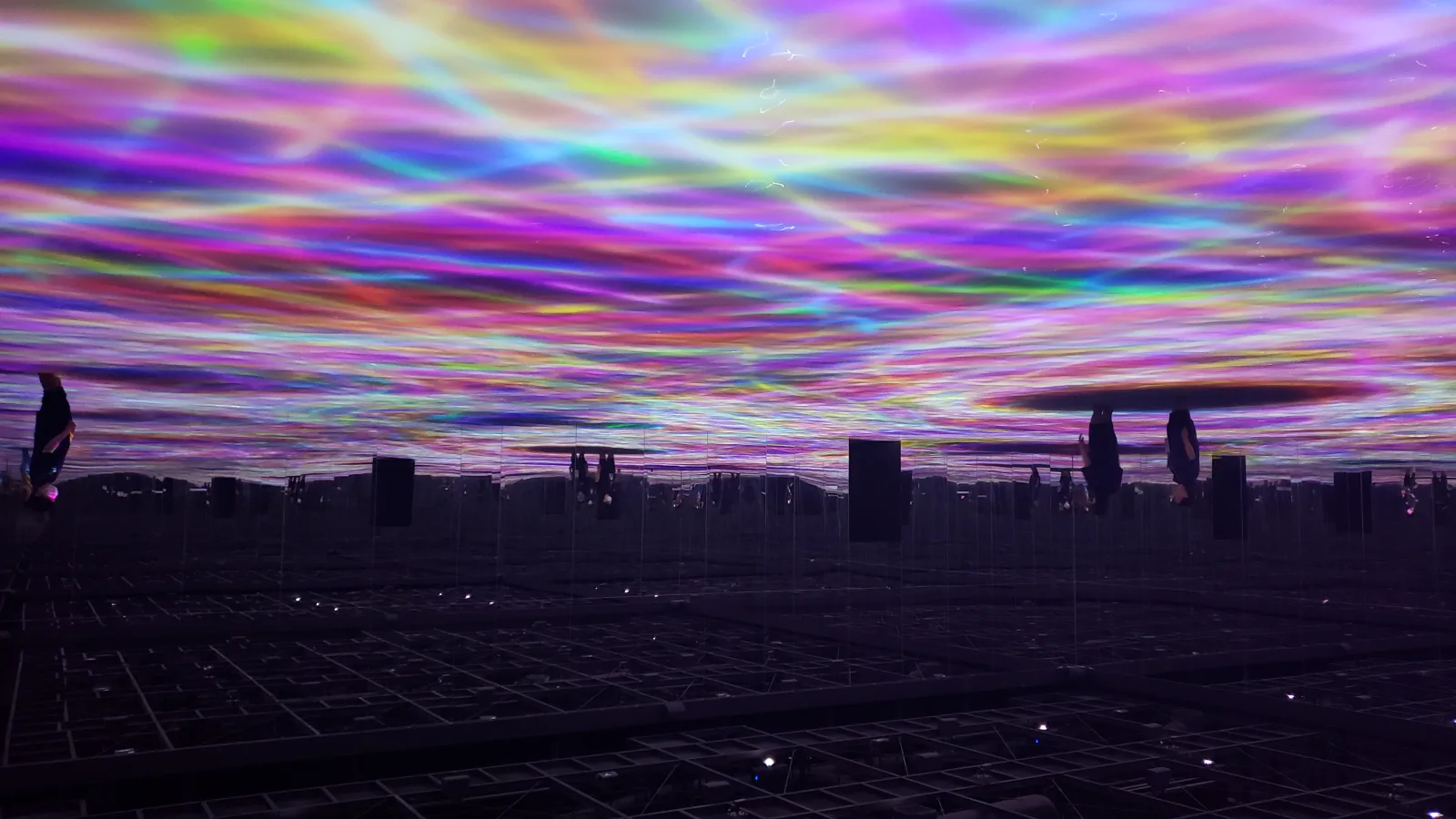 Una instalación de luz inmersiva y colorida en teamLab Planets, reflejada en el suelo de espejo